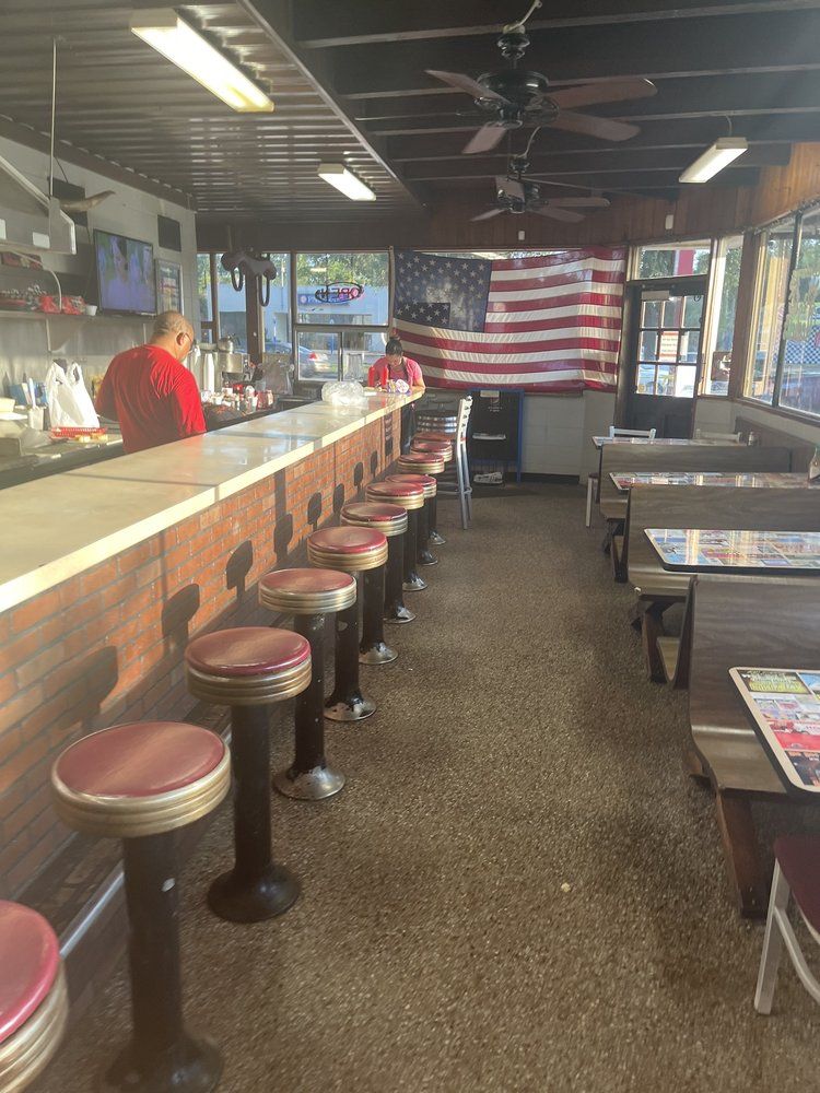 The long lunch counter with red-topped chrome stools, booths along the windows and an American flag on the back wall